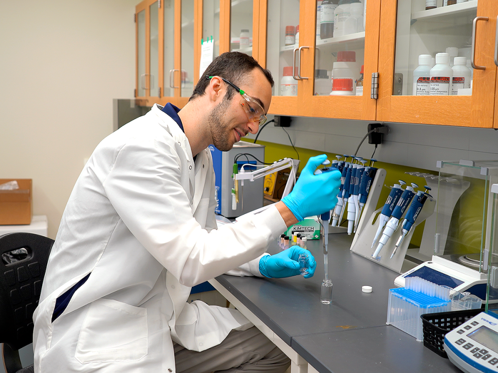 Adam Smerigan working in his lab wearing a white lab coat and blue gloves