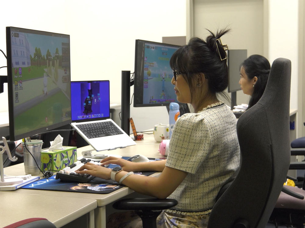 Two young women seated at computers and playing video games