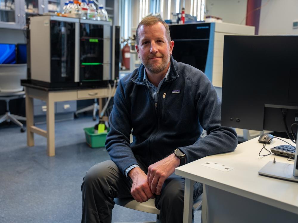 A man sitting at a lab desk with research equipment surrounding him.