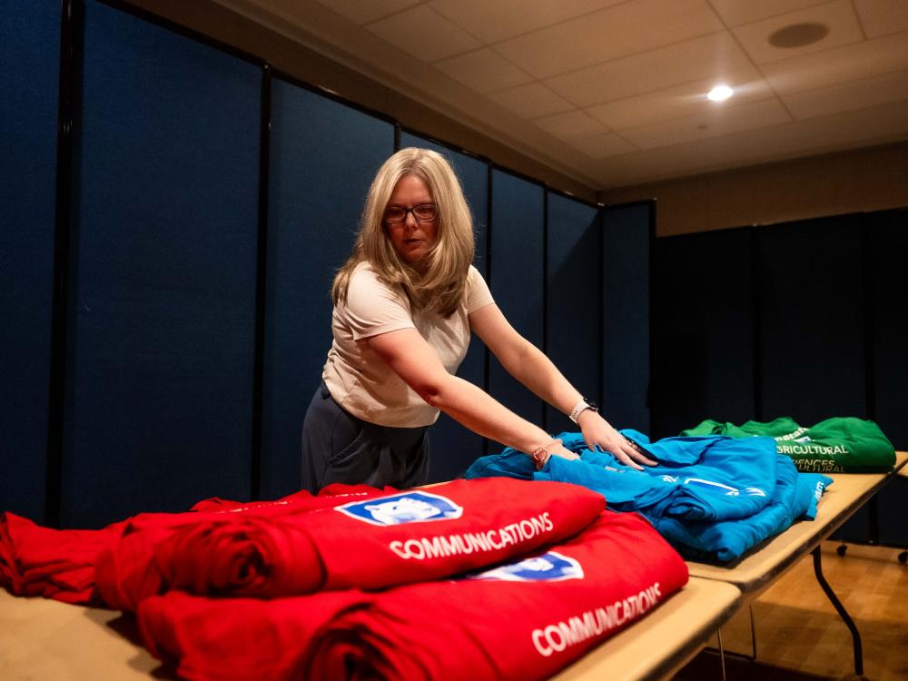 A woman folds colorful t-shirts and arranges them on a table