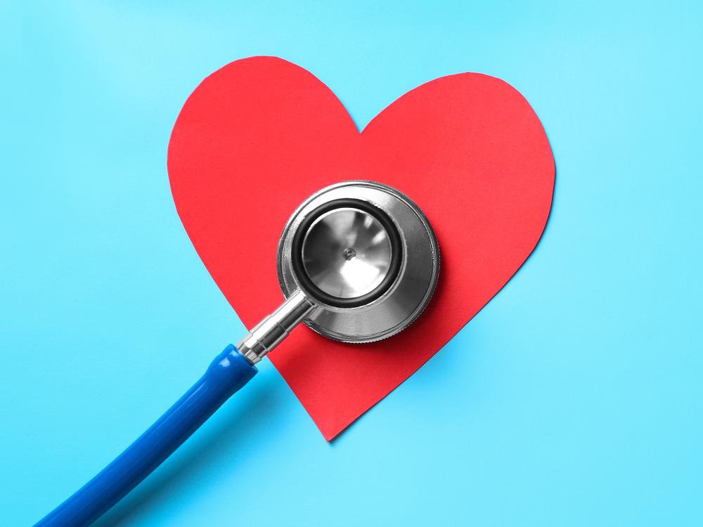 A stethoscope placed on a red paper heart against a light blue background, symbolizing heart health and medical care.