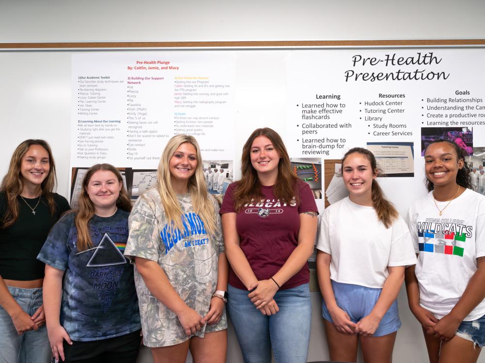 Six people stand in front of a wall of posters