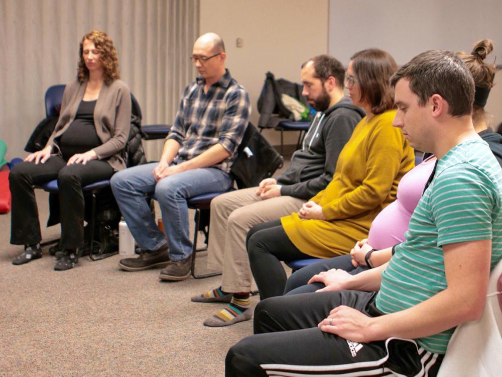 A group of parents sit in a circle with their eyes closed practicing a mindfulness meditation.