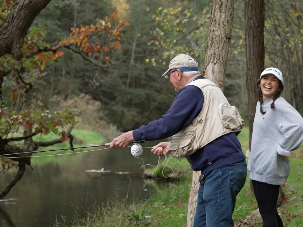 A fisherman reels in a line while a girl to his right laughs