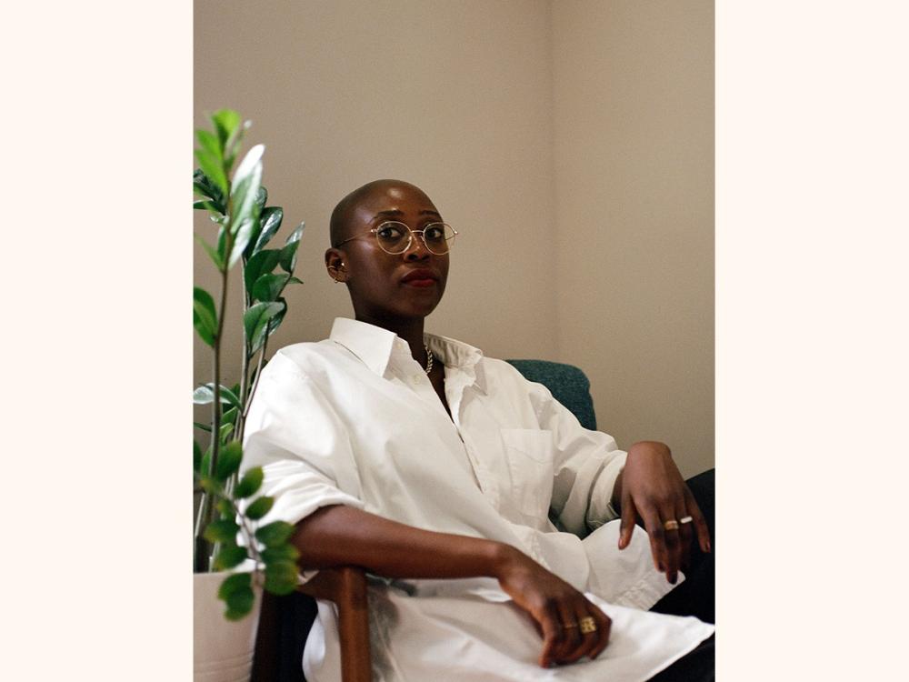 Critically acclaimed author Pemi Aguda sitting on a chair in front of a plant