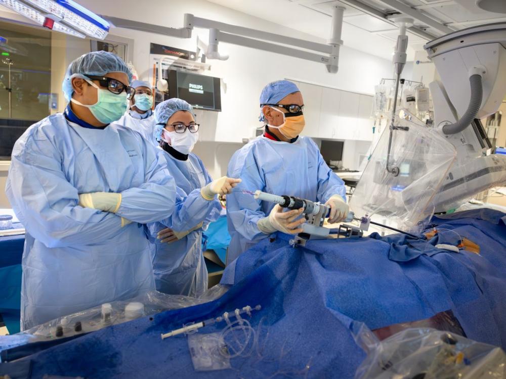 A medical team in full surgical attire, including masks, gowns, gloves, and protective eyewear, perform a procedure in a high-tech operating room.