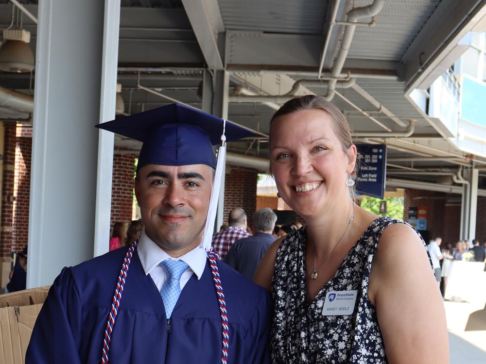 A man wearing a blue graduation gown stands next to a woman at a baseball stadium.