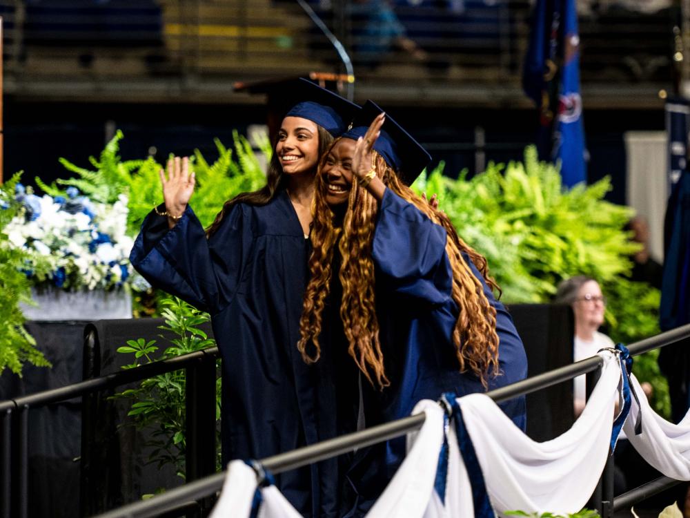 Graduates hugging each other and waving to the crowd