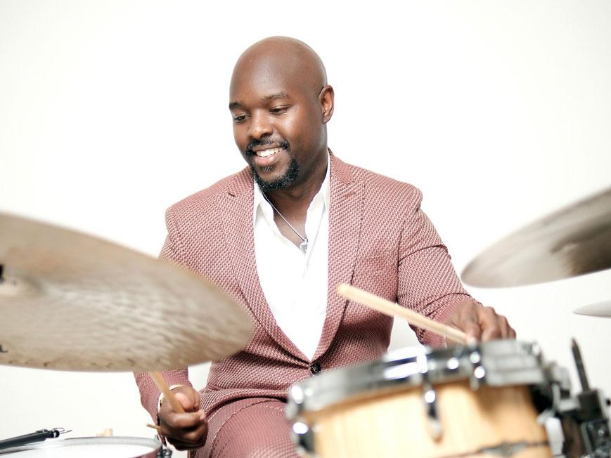 A smiling man wears a suit plays the drums