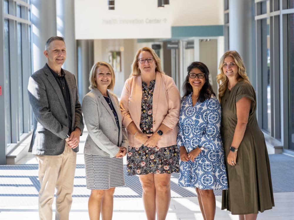 a group of five people posing for a photo in a bright, spacious lobby