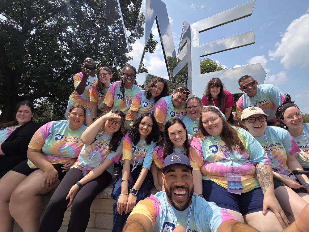 A group of people wearing tie-dye T-Shirts pose in front of a metallic statue.