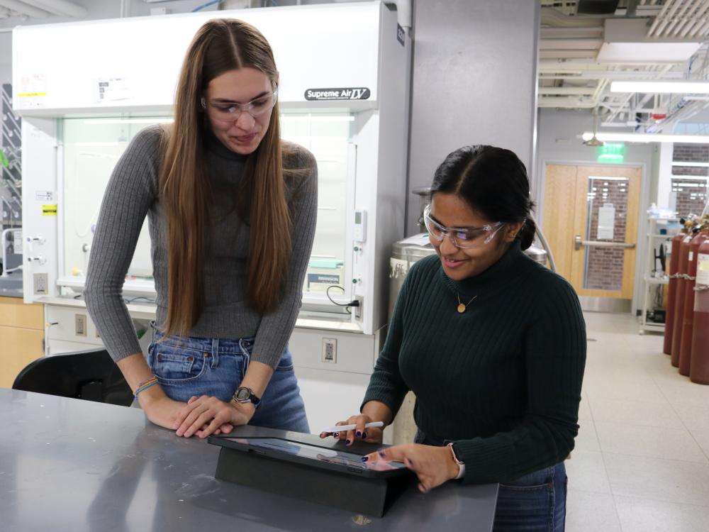 Two students discuss lab sustainability at a table