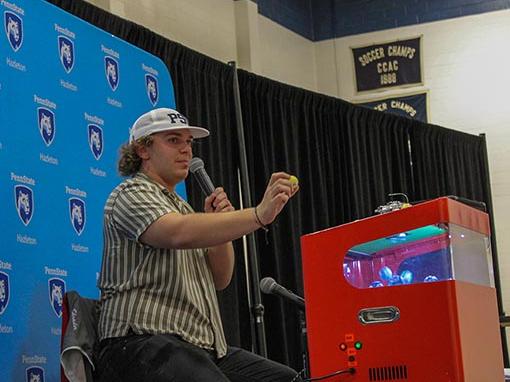 A person sitting on a stage holding a microphone and calling out bingo numbers.