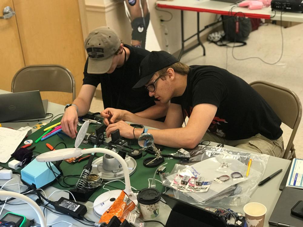 Two people hunched over a work table building a rocket