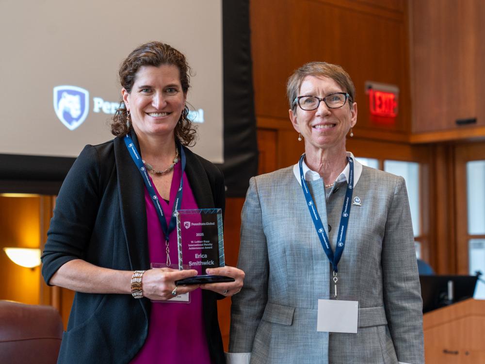 Two women standing next to each other smiling. The woman on the left is holding an award plaque.