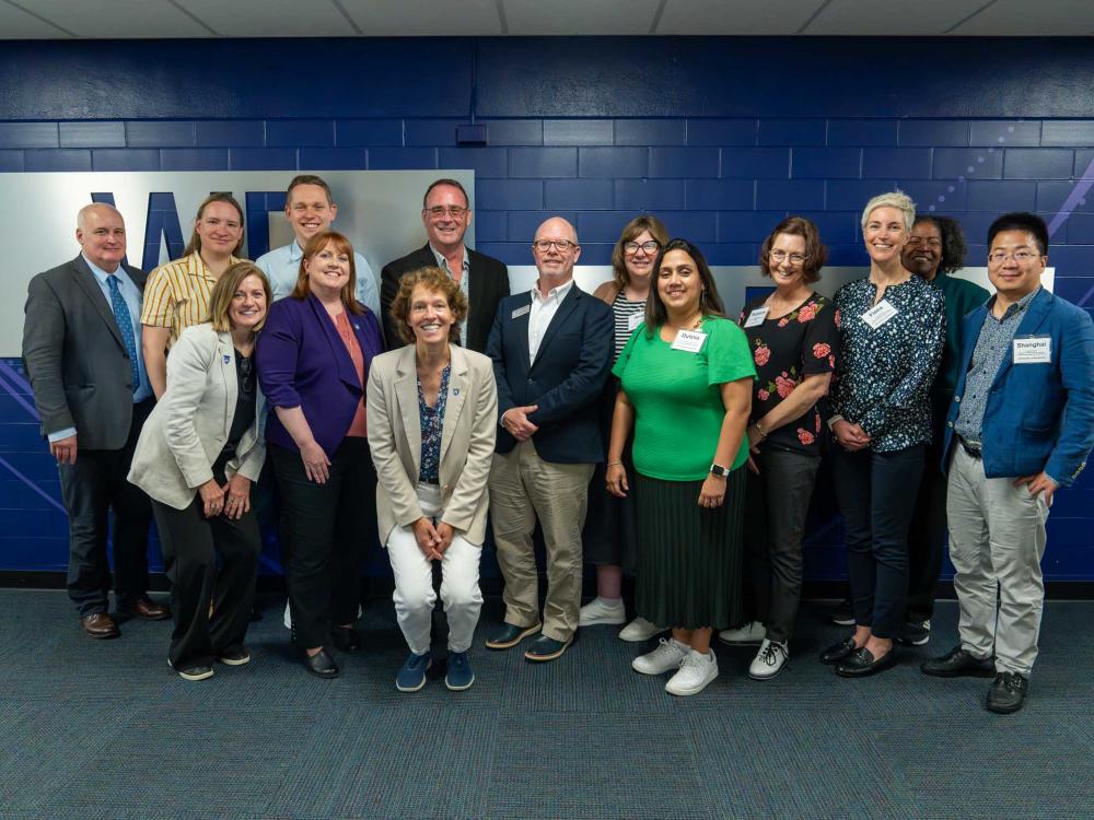 A group of over a dozen faculty members in front of a blue wall