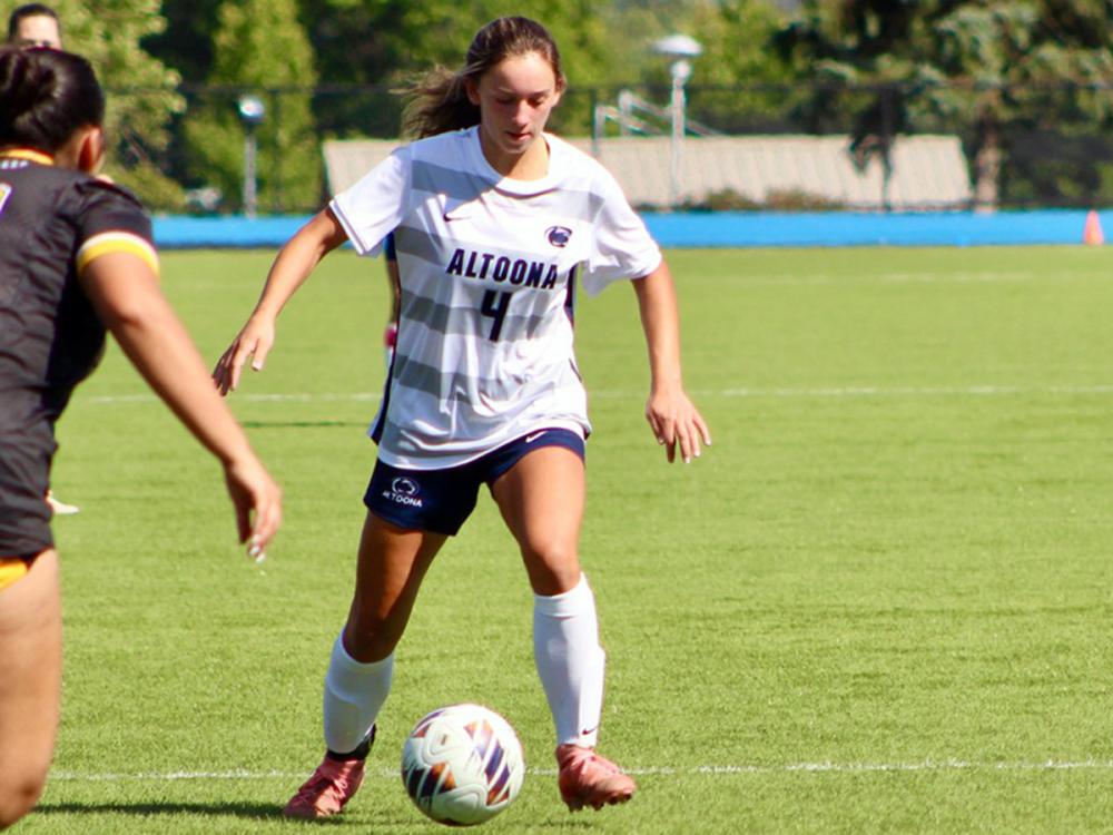 Soccer player in a white Altoona jersey with the number 4 controls the ball on the field during a match.