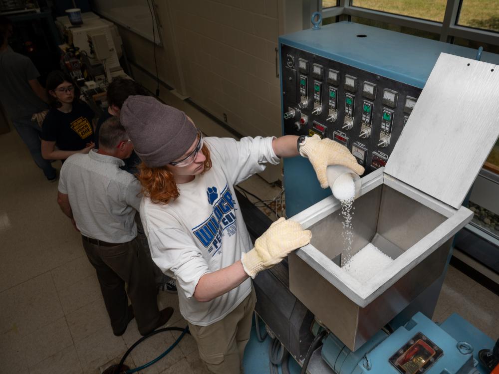 A student adds pellets to an open bin of a machine