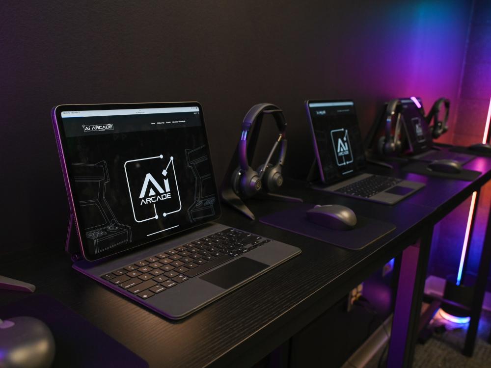 A row of iPads and headphones in the AI Arcade, where students can explore premium AI tools, custom-designed experiences, and retro-inspired games in a futuristic, neon-lit setting.