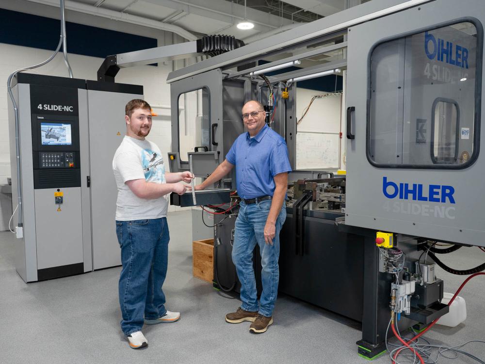 Two people stand in front of a large piece of machinery