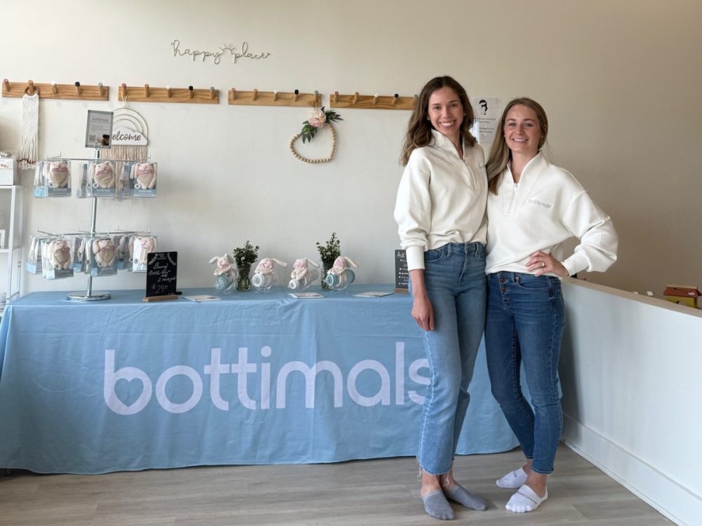 Julianne and Jill stand in front of a Bottimals product table