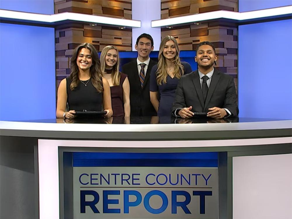 Five students standing behind a newscast desk