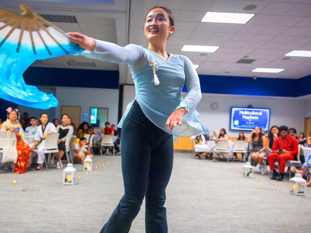 Sandy Zeng performs a Chinese fan dance, her outstretched arm holding a flourishing fan.