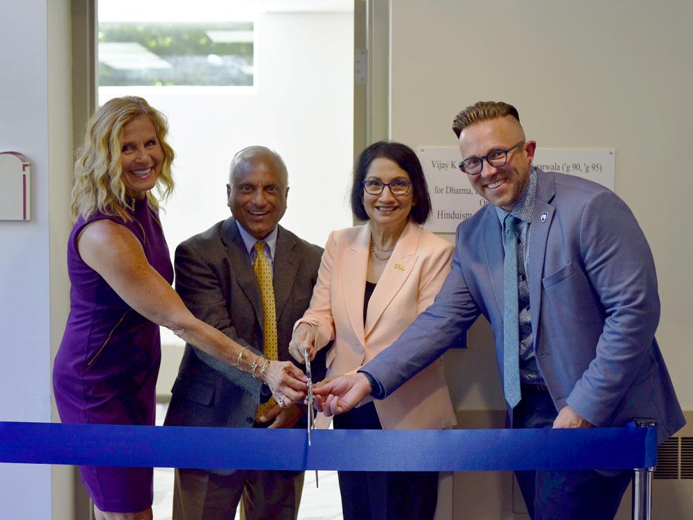 Four smiling people cut a large blue ribbon with large scissors
