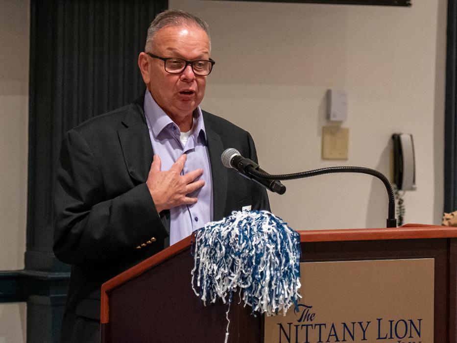 Man in a dark coat and blue dress shirt with his hand on his chest behind a lectern