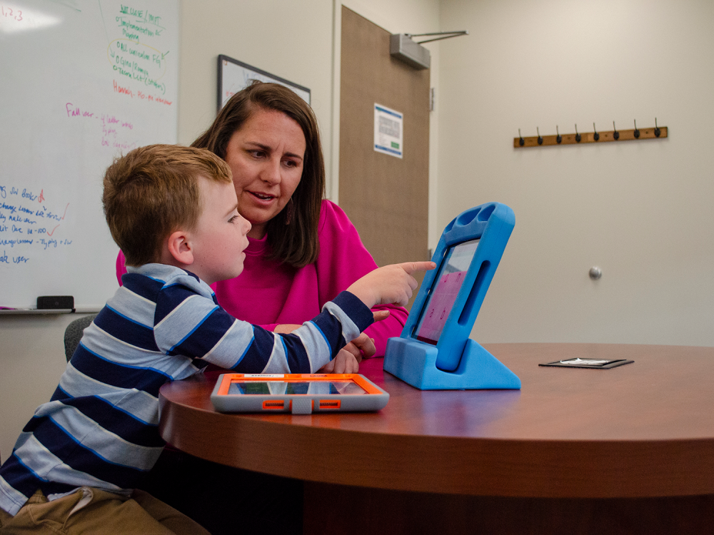 Jessica Caron working with a young child on an augmentative and alternative communication tablet.
