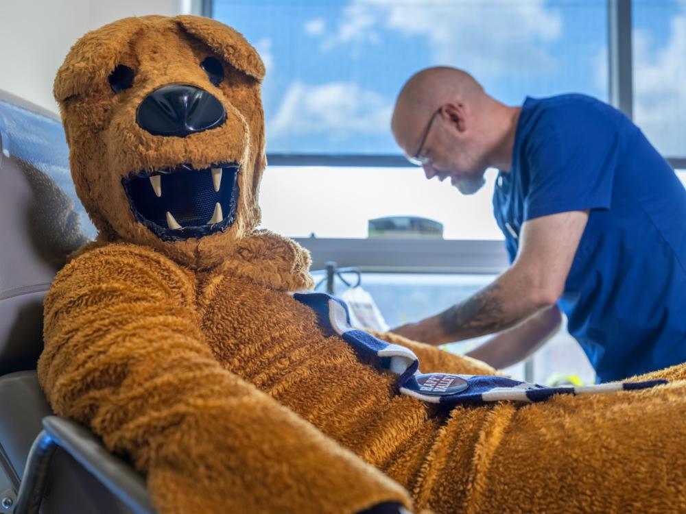 The Nittany Lion sits in a chair as a nurse administers a vaccination at University Health Services
