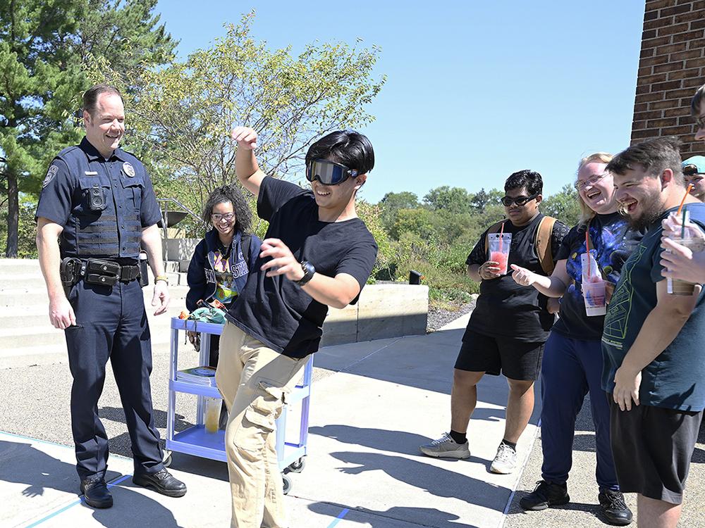 A student wearing goggles walks along a blue taped line as a police officer watches.