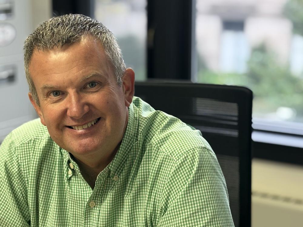 Man in green button-down shirt smiles in front of foggy window.
