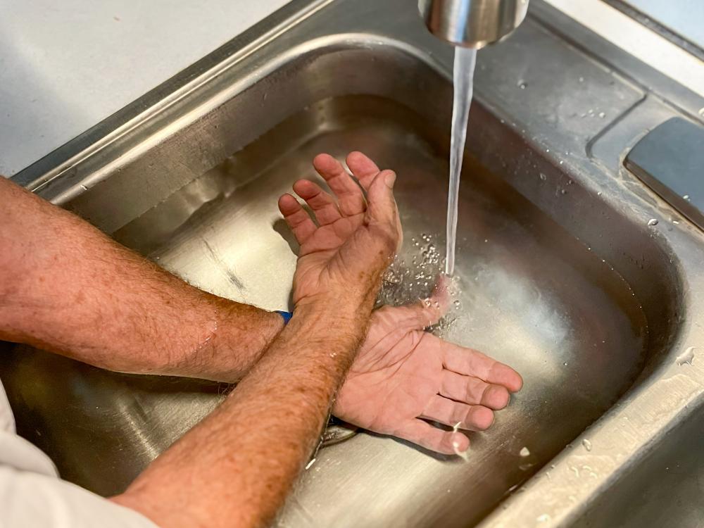 The arms of an older person rest in a sink that is filling with water