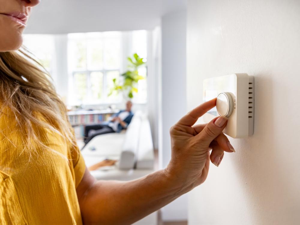 A person adjusts a thermostat on a wall
