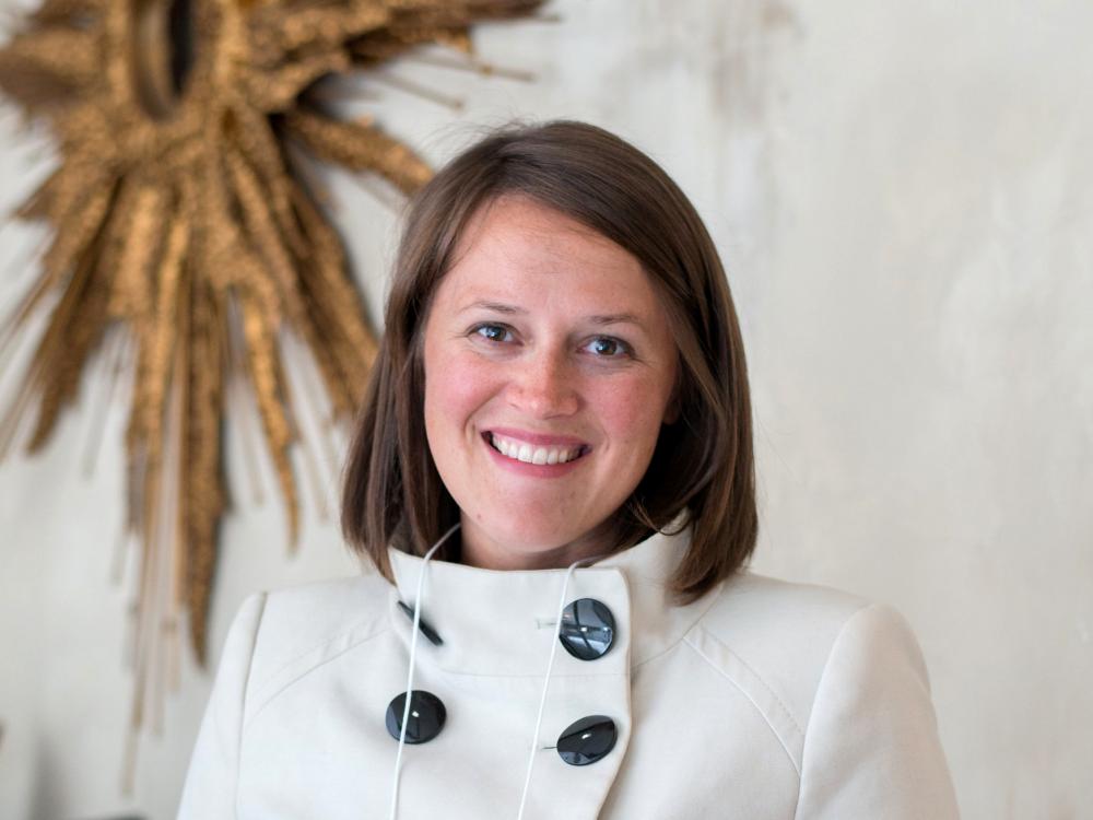 Headshot of Amanda Hellman with a piece of sunburst artwork on the wall behind 