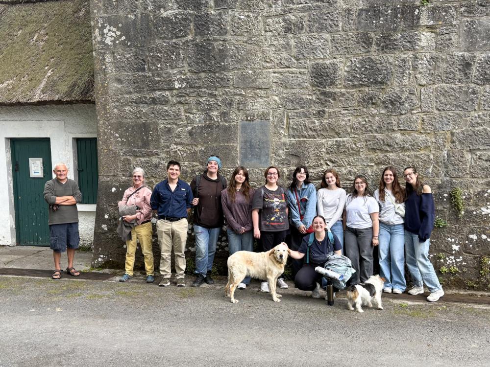 Penn State students and faculty and two dogs stand in a row outside the Norman Tower in Thoor Ballylee, Ireland.