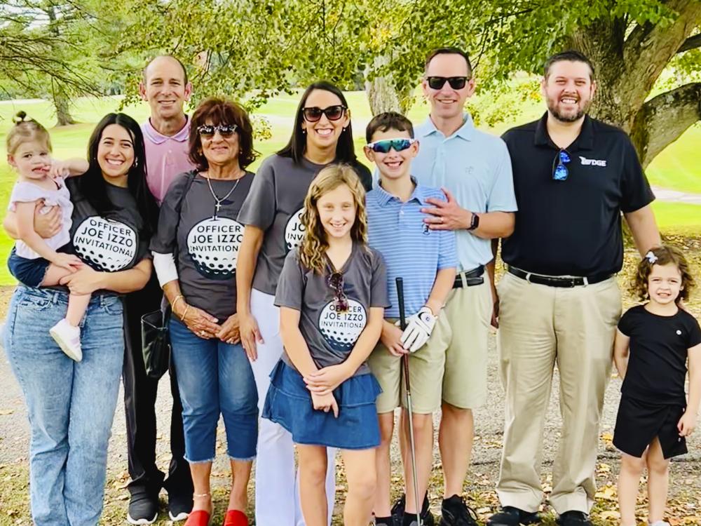 Family photo of ten people posing for a photo under a tree with a golf course in the background