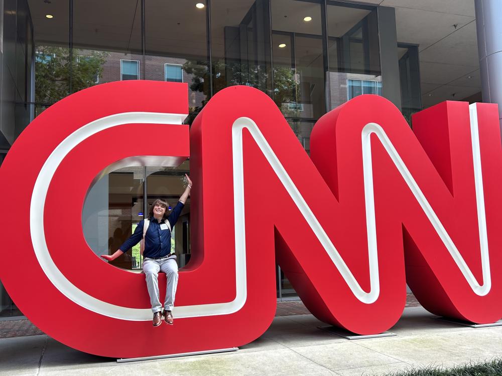 Luke Snyder sitting and waving in a giant CNN logo