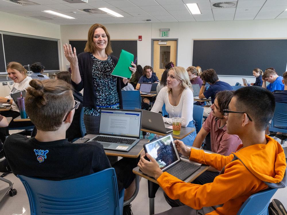 A professor stands and smiles as she talks to a group of seated students