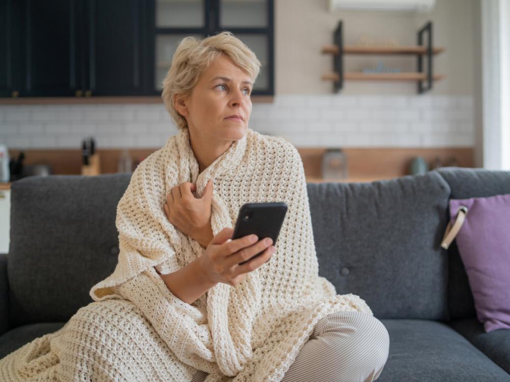 A person sits in their living room on a couch, with a blanket wrapped around them
