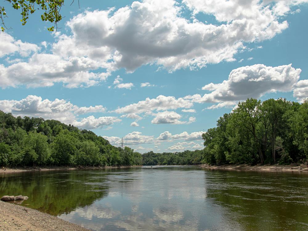 wide clear river with trees on banks and blue sky above