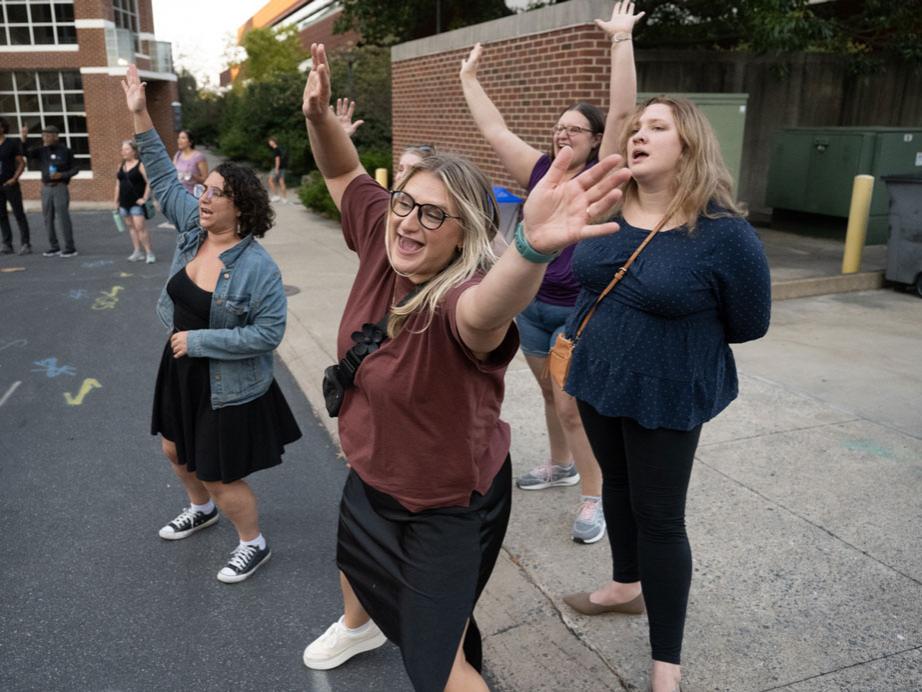 A group of young women sing and dance at an outdoor concert.