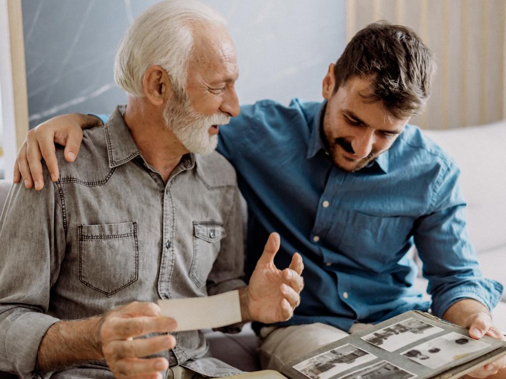 A man in his 70s talks fondly to a man in his 30s while they look at an old photo album