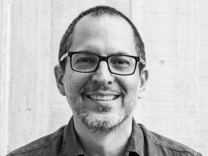 Black and white head shot of a man with a dark hair and black-rimmed glasses