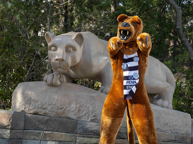 A person in a lion costume standing in front of a lion statue.