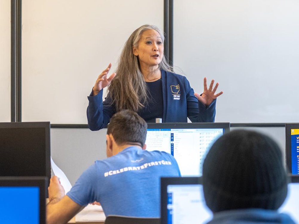 Mahli Xuan Mechenbier, wearing a navy blazer, speaks to a classroom of students seated at computer stations at Kent State University.