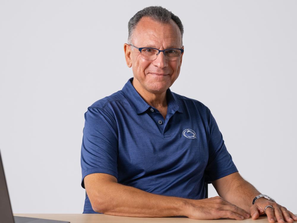 Fotis Sotiropoulos sits at a table with a laptop to the left with a white wall behind him.