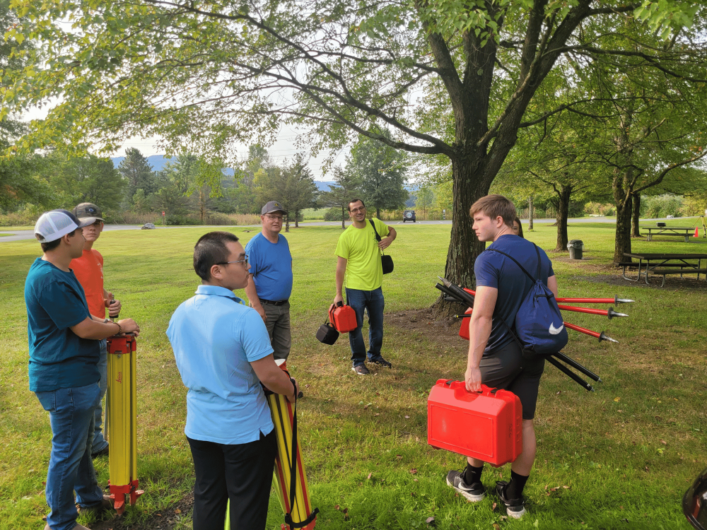A group of people, including surveying engineering students, gather in a park