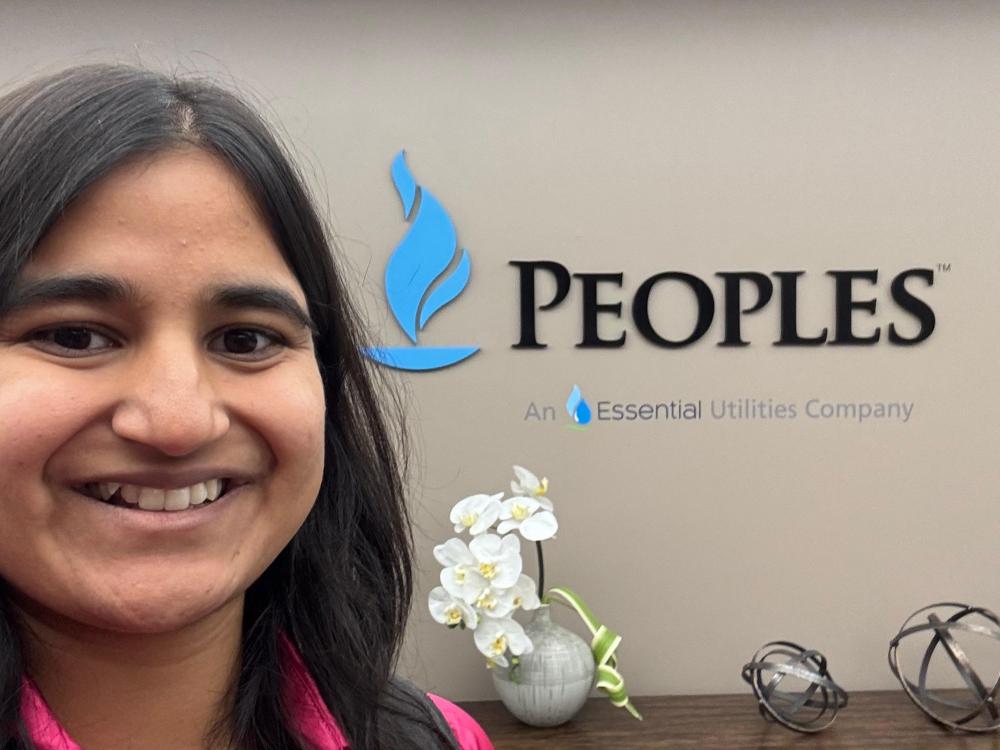 A photo of a student smiling in an office and on the wall in background is a Peoples gas logo